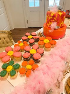 a table topped with lots of cupcakes covered in frosting and pink feathers