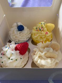 four cupcakes in a box with white frosting and fruit toppings on them