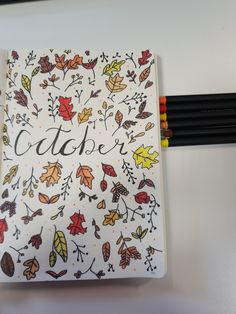 an open notebook with autumn leaves and the word october written in cursive writing