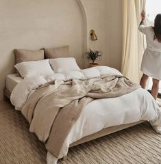 a woman standing in front of a bed with white sheets and blankets on top of it