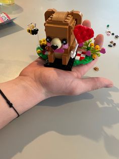 a hand is holding a small toy house made out of legos on a table