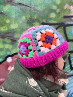 a woman wearing a pink and green crocheted hat with flowers on the side