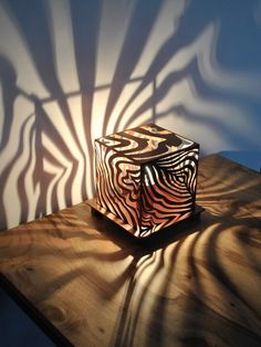 a wooden box sitting on top of a table next to a shadow cast by a wall