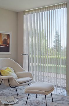 an egg chair and ottoman sit in front of a window with vertical blinds on the outside