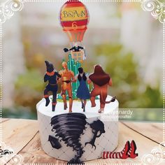 a birthday cake decorated with figurines of people and hot air balloon in the sky