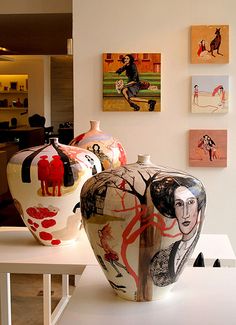 two vases sitting on top of a white table in front of pictures and paintings