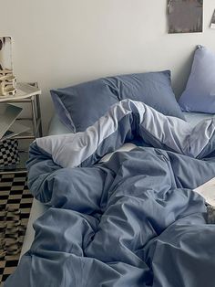 an unmade bed with blue sheets and pillows on top of it in a bedroom