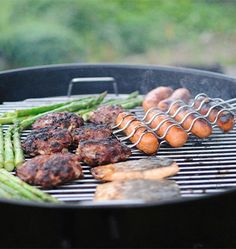 an outdoor grill with hot dogs, asparagus and other foods cooking on it