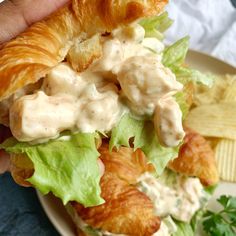 a croissant sandwich with lettuce and chicken salad on it, being held up by someone's hand