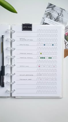 an open planner book with several photos and pens on the pages, next to a plant