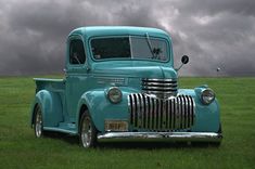 an old blue truck is parked on the grass in front of some dark storm clouds