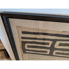 an art piece with black and white designs hanging on the side of a wooden frame