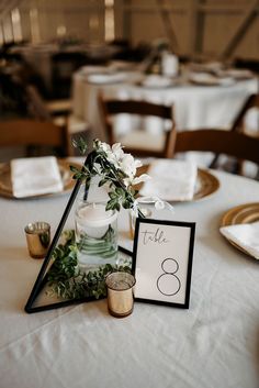 the table is set up with white flowers and greenery in glass vases on top