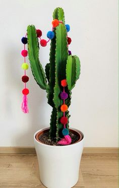 a cactus with colorful pom - poms in a white pot