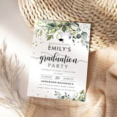 a white graduation party card with greenery on it next to a straw hat and wicker basket