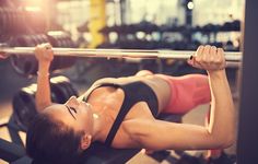 a woman laying on the ground with a barbell in her hand and looking up