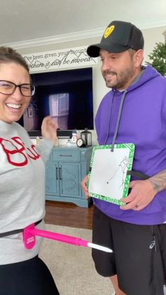 a man and woman are standing in the living room holding a pink toothbrush with a drawing on it