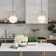 a kitchen with white counter tops and gold trim around the edges, along with two hanging lights