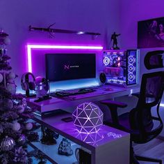 a computer desk topped with a monitor next to a christmas tree in a room filled with purple lights