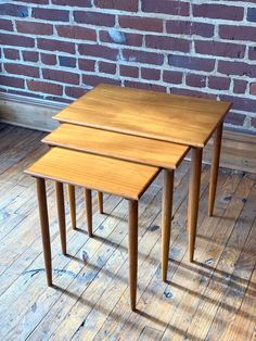 two wooden tables sitting on top of a hard wood floor next to a brick wall