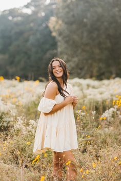 a woman standing in a field full of flowers smiling at the camera with her arms crossed