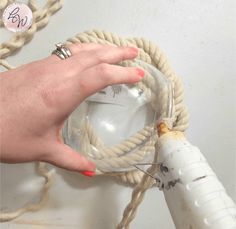 a woman's hand is holding a glass with some rope on the wall behind her