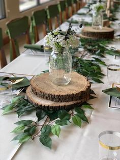 the table is decorated with greenery and glass vases filled with white flowers on wood slices