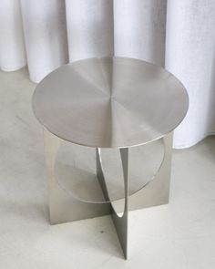 a round metal table sitting on top of a white floor next to a pair of curtains