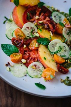 a white plate topped with cucumbers, tomatoes and other vegtables