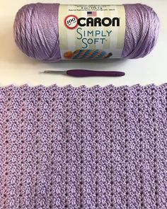 a crocheted purple blanket next to a ball of yarn and a knitting needle