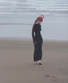 a woman standing on top of a sandy beach next to the ocean wearing a black dress