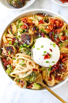 two bowls filled with pasta and vegetables on top of a white countertop next to utensils