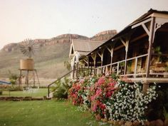 a house with flowers in the front yard and mountains in the backgrouund