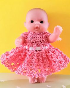 a baby doll wearing a pink crochet dress and holding her hand in the air