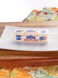 a piece of cheese sitting on top of a white plate next to a wooden cutting board