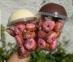 two plastic containers filled with pink frosted donuts in front of a white wall