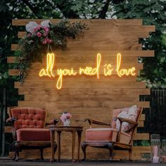 two chairs sitting next to each other in front of a wooden wall that says all you need is love