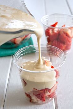 strawberries and cream are being poured into small plastic cups on a white wooden table