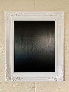 a white frame hanging on the wall with a black background in front of an empty brick wall