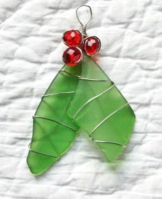 a green leaf with two red beads hanging from it's side on a white surface