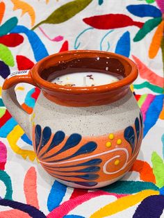 an orange and white vase sitting on top of a colorful table cloth next to a candle