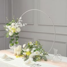 a table topped with white flowers and candles next to a vase filled with greenery