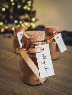 two small jars filled with cookies on top of a wooden table next to a christmas tree