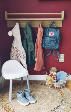 a white chair sitting in front of a red wall next to a wooden coat rack