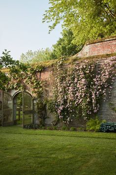 an old brick building with vines growing on it's side and a green lawn in front