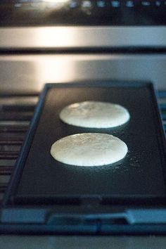 two uncooked pizzas sitting on top of an oven