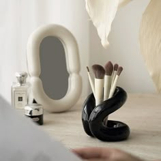 there is a vase with makeup brushes in it on the table next to a mirror