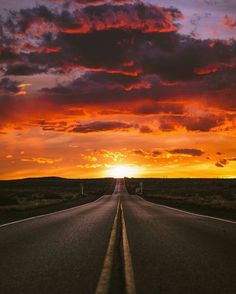 the sun is setting on an empty road in the middle of nowhere, with dark clouds