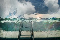 the reflection of clouds in the water and ladders leading up to the bottom of the pool