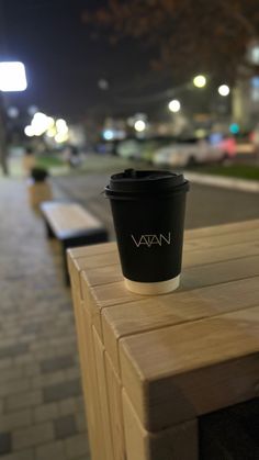 a coffee cup sitting on top of a wooden table next to a park bench at night